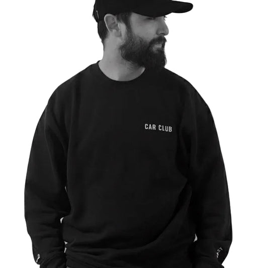Man wearing a black 'Car Club' sweatshirt and cap against a light tiled wall.